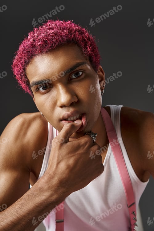 Preview: portrait of stylish pink haired man with hand on his face and lip looking at camera, fashion concept