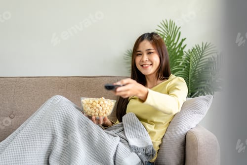 Preview: Young asian woman is watching movie on television and holding re