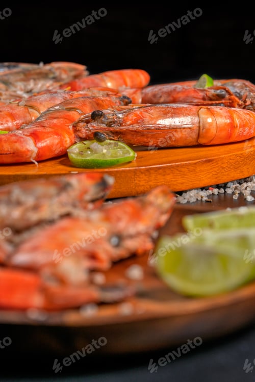 Preview: Cooked prawns with lime wedges on wooden plate, seafood gastronomy