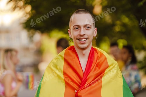Preview: White man smiling and holding rainbow flag during pride parade at city