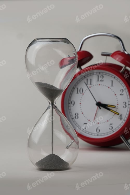 Preview: Glass hourglass and an old-fashioned alarm clock depicting the passage of time