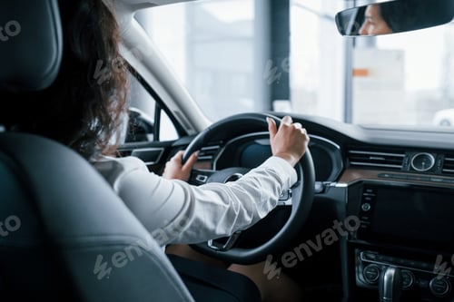 Preview: Hands on steering wheel. Beautiful businesswoman trying her new car in the automobile salon