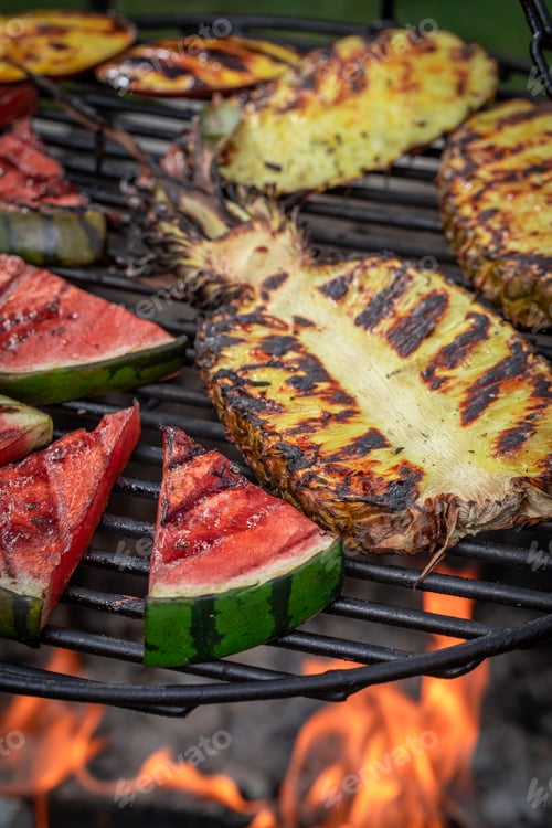 Preview: Hot roasted watermelon and pineapple on bonfire with flames.
