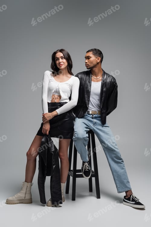 Preview: full length of woman in stylish outfit and young african american man in leather jacket posing