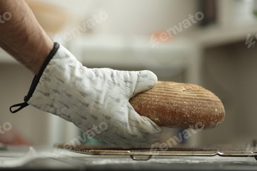 Preview: The man holds the freshly baked bread in his hands with gloves