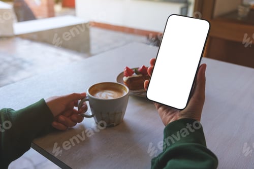 Preview: A woman holding mobile phone with blank screen while drinking coffee and eating dessert in cafe