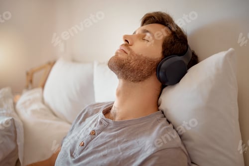 Preview: Relax. calm and resting man listening to music on his wireless headphones while relaxing on his bed