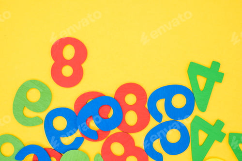 Preview: Flat lay of colorful wooden numbers on a yellow surface - space for text