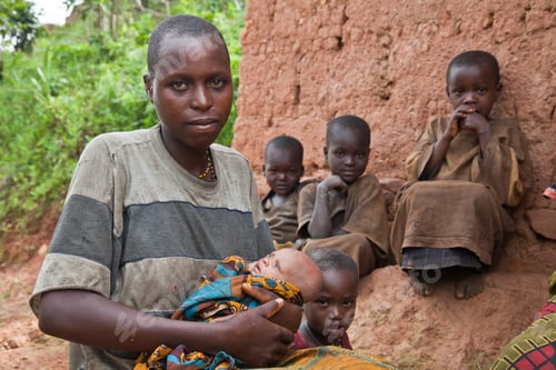 Preview: Mother holding a baby with children sitting by a mud wall