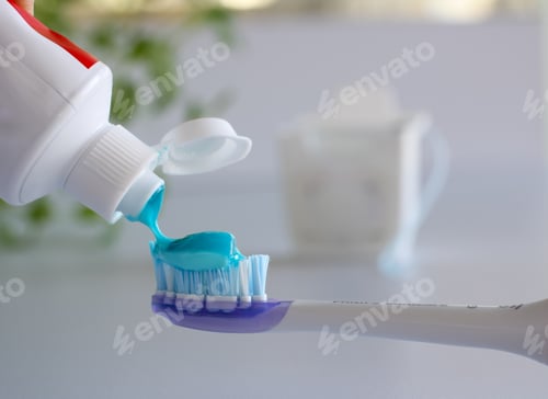 Preview: Person putting toothpaste on toothbrush with dental floss in background for dental hygiene concept