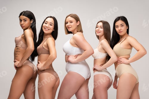 Preview: five pretty multiethnic girls in lingerie posing at camera with hands on hips isolated on grey, body