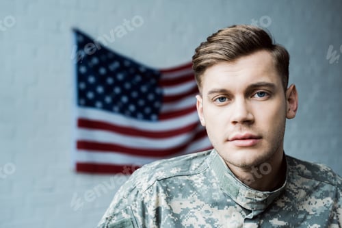 Preview: handsome man in military uniform looking at camera near american flag