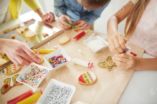Preview: Hands of boy, his sister and mother decorating easter biscuits at kitchen counter