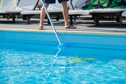 Preview: Male cleaning outdoor swimming pool with underwater vacuum tube