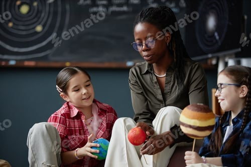 Visualização: Mulher negra ensinando diversas crianças sobre planetas em sala de aula