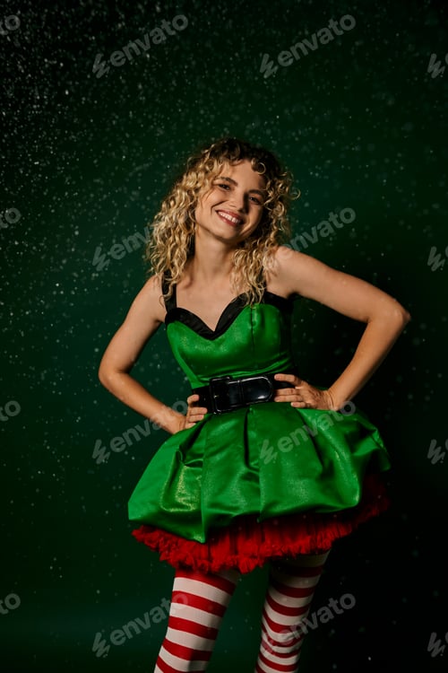 Preview: cheerful woman in green festive dress smiling and holding hands akimbo, new year elf concept