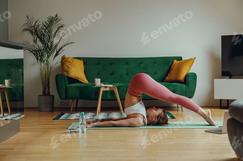 Preview: A woman practices yoga on hardwood flooring in a living room with a green couch