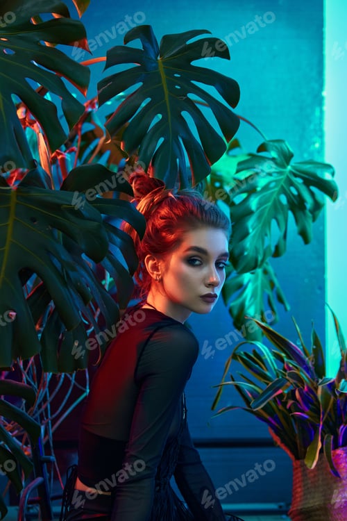Preview: Young woman surrounded by vibrant tropical plants, wearing black leather outfit and long-sleeved