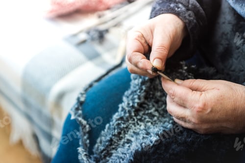 Preview: Closeup shot of a woman sitting on the couch at home and knitting a gray and black scarf