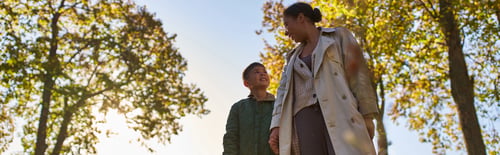 Preview: african american mother and child in outerwear holding hands near trees in autumn park, fall, banner