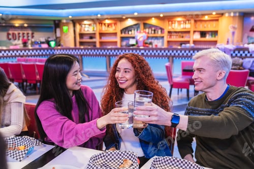 Preview: Happy friends toasting drinks in a bowling alley restaurant