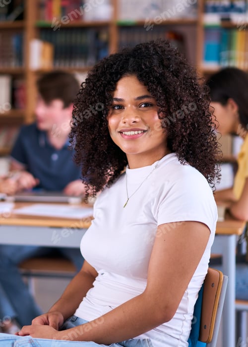 Preview: Portrait happy young Latin female student sitting in library with classmates in background.
