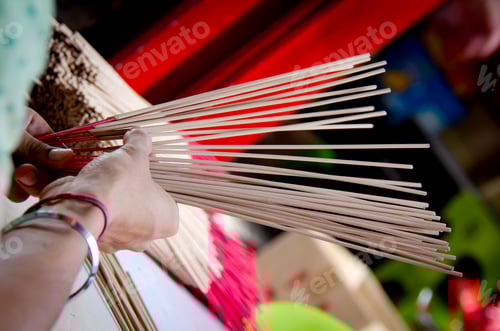 Preview: Hands holding and arranging incense sticks with red bases