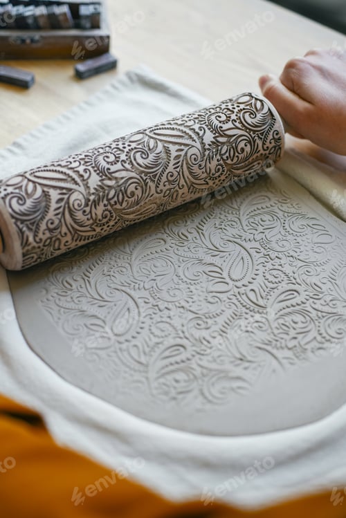 Preview: Woman's hands with patterned rolling pin, decorating layer of clay