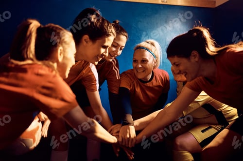 Preview: Happy female soccer players holding hands in unity in locker room.