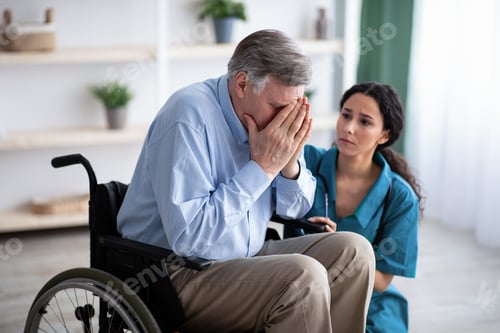 Preview: Depressed senior man in wheelchair crying, young doctor trying to help him at retirement home