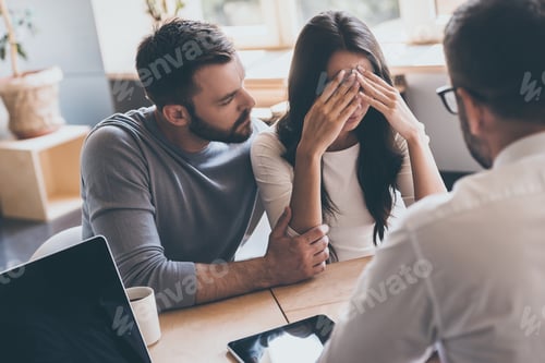 Preview: Bad news. Young man comforting his wife while sitting together with psychologist