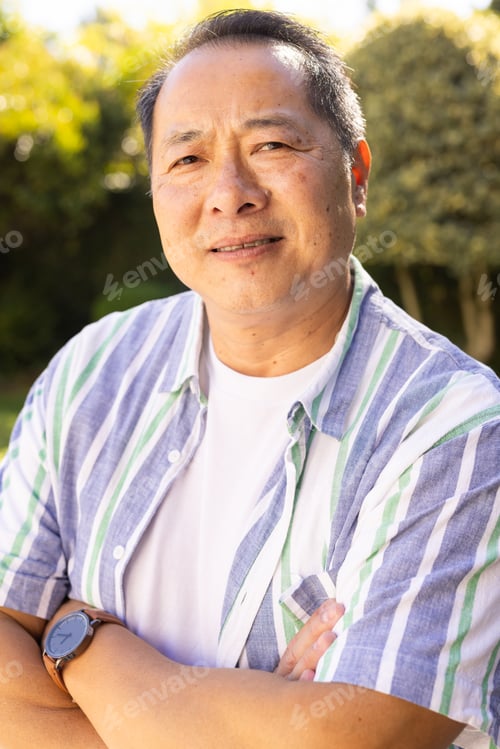 Preview: Smiling asian middle-aged man in striped shirt standing outdoors, enjoying sunny day