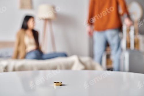 Preview: selective focus of wedding ring on table near interracial couple quarreling in bedroom, divorce