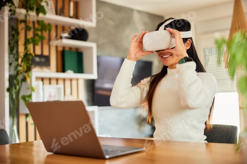 Preview: A smiling female influencer using a VR headset, sitting in front of the laptop.