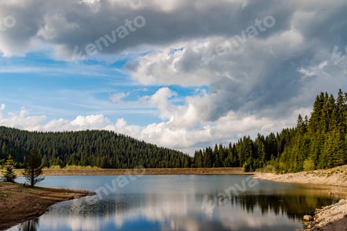 Preview: Lake with clear water and stone shore in spruce forest with fir trees against a daytime sky