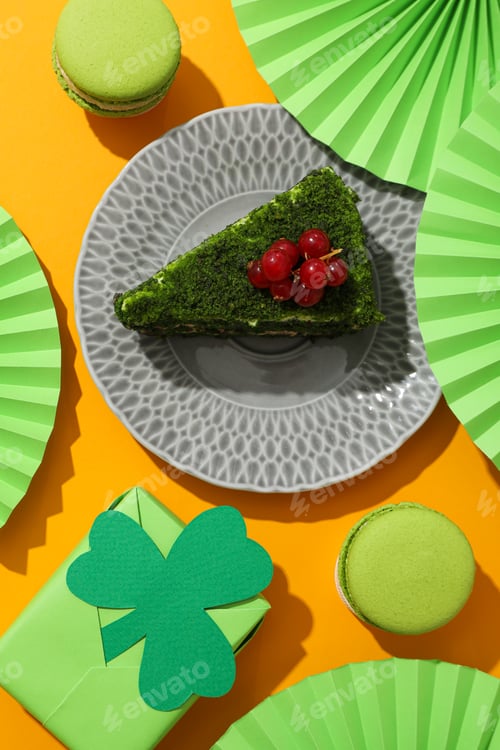 Preview: Piece of cake on plate, macaroons and box with clover on yellow background, top view