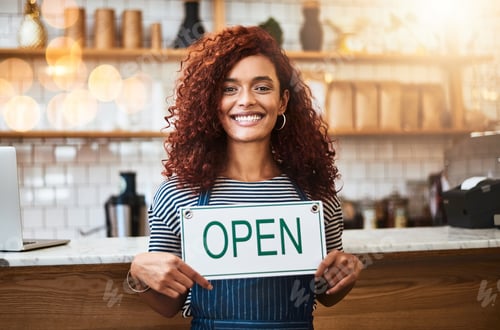 Preview: Service with a big smile. Portrait of a young woman holding up an open sign in her store.