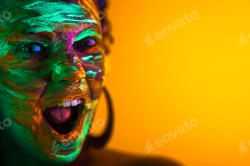 Preview: girl with fluorescent paint makeup. Dye glowing near UV light. Woman with open mouth in neon light.