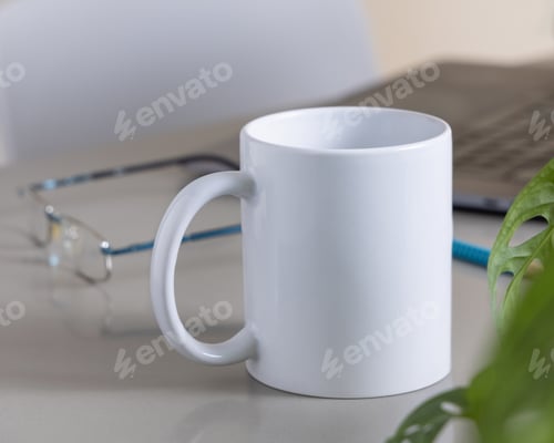 Preview: White coffee mug on grey office table against laptop, glasses and plant closeup, mockup