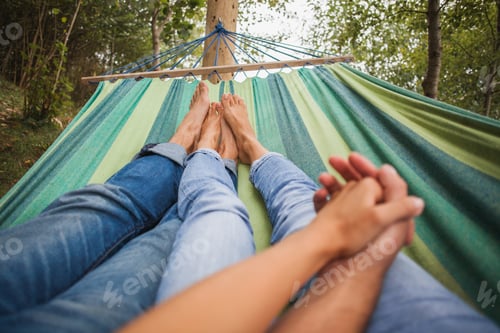 Preview: man and woman in love lying in hammock embracing, holding hands together, legs close-up
