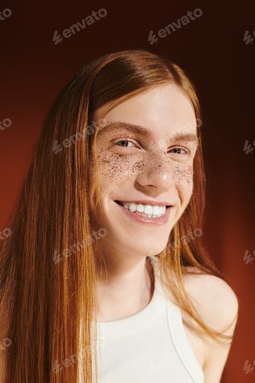 Preview: Young and stylish individual with bright red hair smiles confidently against a warm backdrop