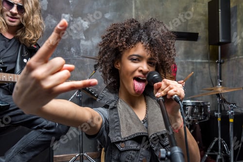 Vista previa: woman with microphone showing rock sign in studio, rock and roll girl concept