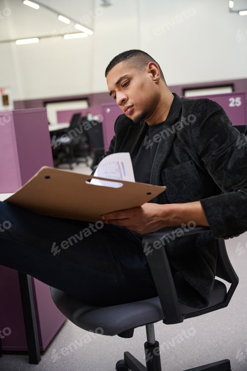 Preview: Focused young man sitting on chair and holding opened folder