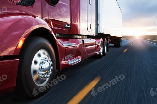 Preview: Close up 3/4 angle view of the cab and front tire on a commercial truck on the road at sunset.