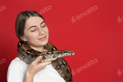Preview: Young woman with boa constrictor on red background, space for text. Exotic pet