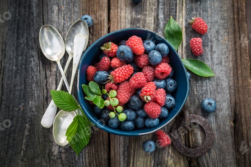 Preview: Top view of blueberries and raspberries in dark blue bowl