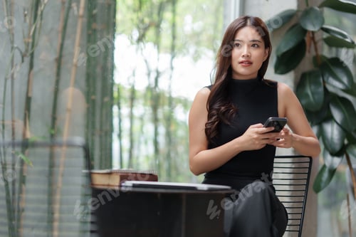 Preview: Businesswoman using smartphone in modern office with bamboo background
