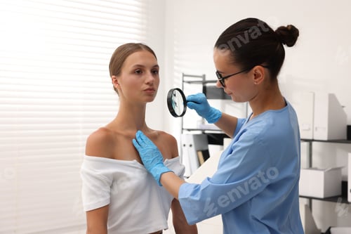 Preview: Doctor examining young woman's mole with magnifying glass in hospital