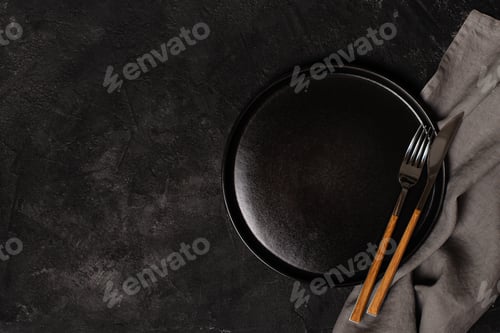Preview: Empty black plate with tableware and napkin on textured dark stone background