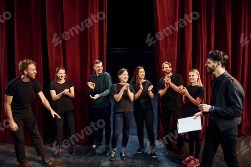 Preview: Man is practicing his role. Group of actors in dark colored clothes on rehearsal in the theater